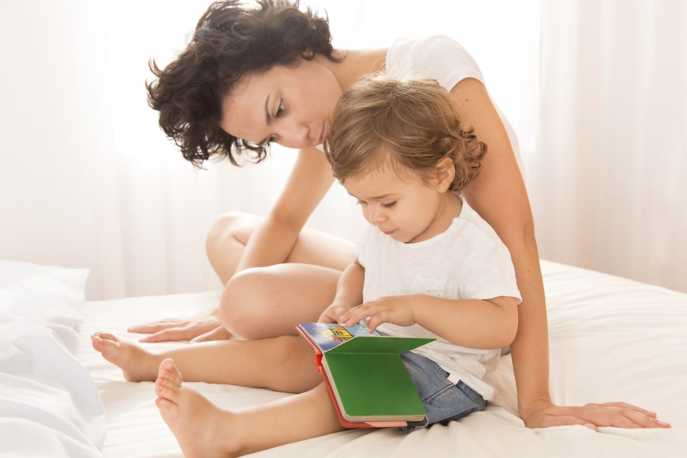mother and child on bed looking at board book