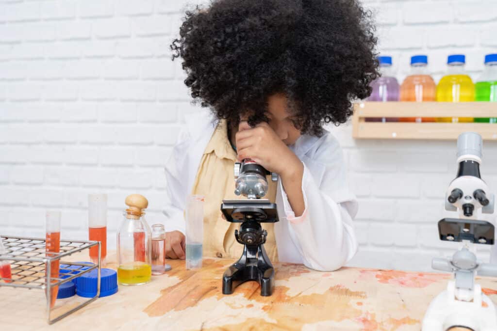 young girl dressed as scientist looking at microscope