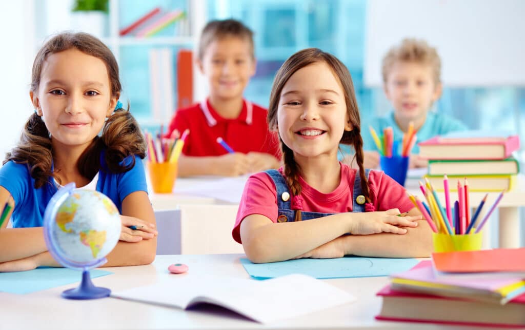 Portrait of two diligent girls looking at camera at workplace with schoolboys on background